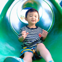 Little Asian Kid Playing Slide At The Playground